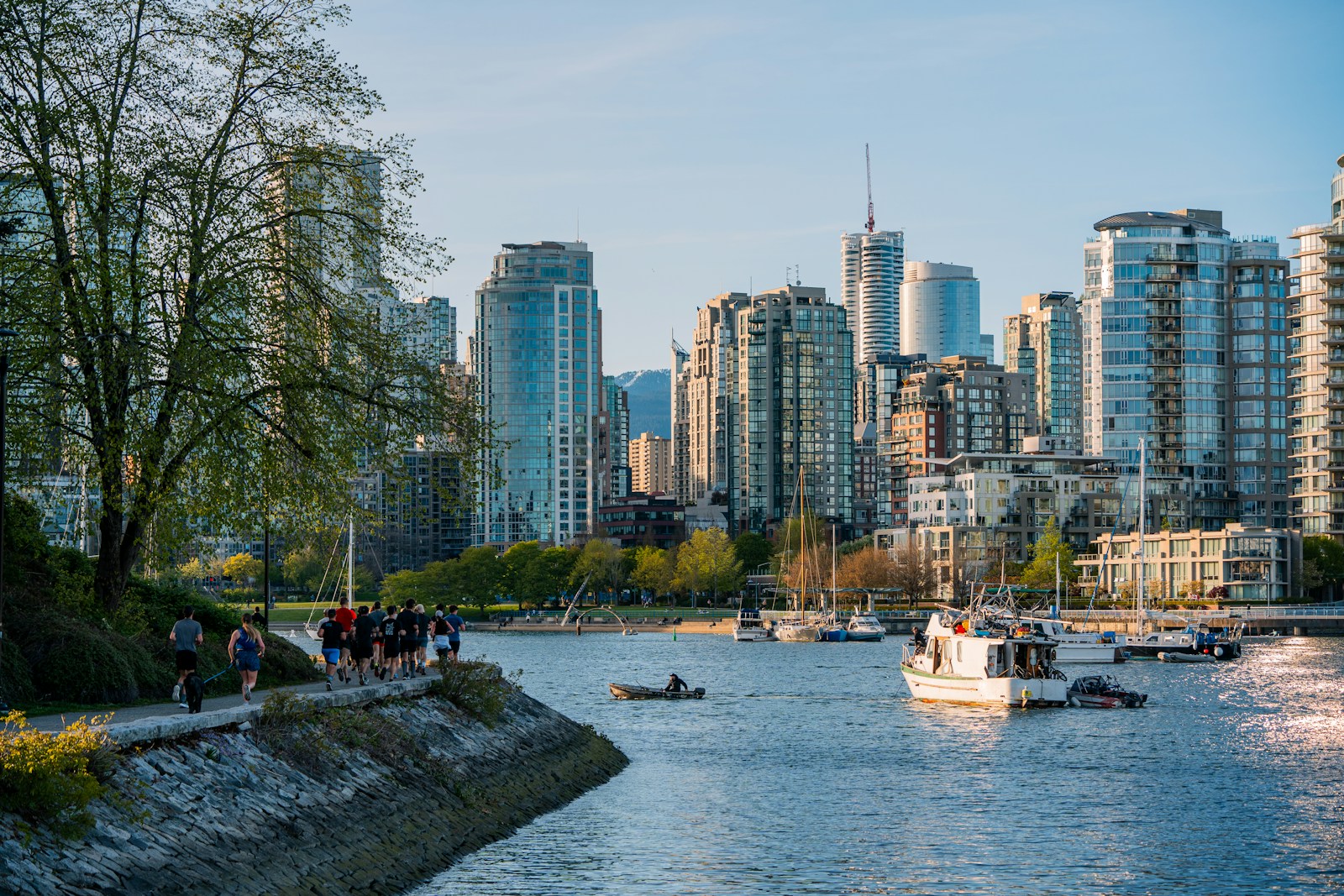 Runners on the False Creek seawall with Yaletown's condo towers and moored boats across the water